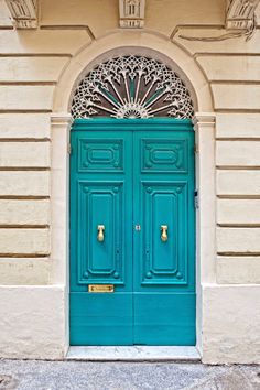 a green door with ornate iron work on the top and bottom, in front of a yellow building