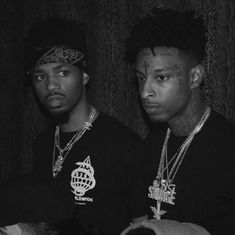 two young men standing next to each other in front of a wall with chains on it