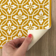 a hand is pressing the corner of a yellow and white wallpaper with an intricate design