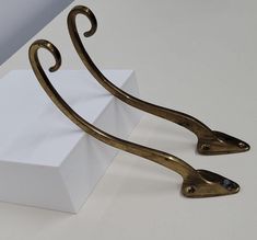 a pair of gold metal brackets on top of a white box with a black object in the background