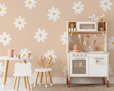 a child's play kitchen with white flowers on the wall and wooden stools