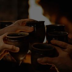 two people holding cups in their hands while sitting at a table with fire behind them