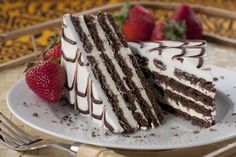 two slices of chocolate cake with white frosting and strawberries on the side sitting on a plate