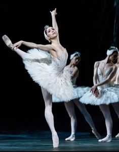 three ballerinas in white tutus and tiaras, one holding a mirror