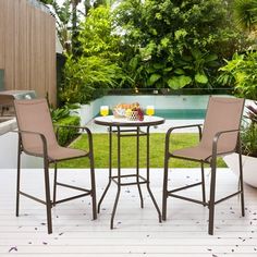 two chairs and a table on a deck in front of a swimming pool with trees