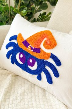 an orange and blue crab pillow on a white couch next to a potted plant