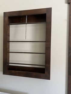 a wooden shelf with a chain hanging from it's side in front of a white wall