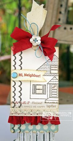 a close up of a card with a red ribbon on it and a house in the background