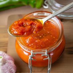 a spoon full of tomato sauce sitting on top of a jar