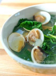 a white bowl filled with broccoli and clams on top of a wooden table