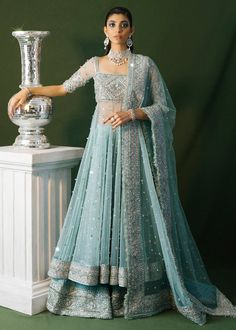 a woman in a blue lehenga standing next to a silver vase and wearing a tiara