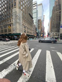 a woman walking across a street in front of tall buildings with cars on the road