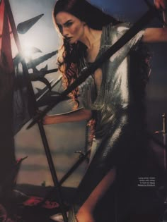 a woman in a silver dress holding two swords and posing for a magazine cover photo