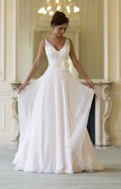 a woman in a white wedding dress standing on the floor with her arms behind her back