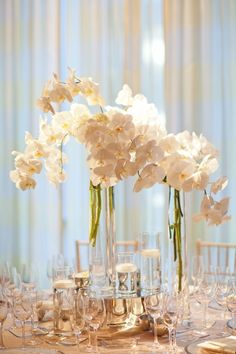 there are many white flowers in the vases on this dining room table set for dinner