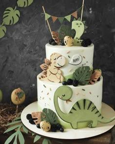 a three tiered cake decorated with dinosaurs and leaves