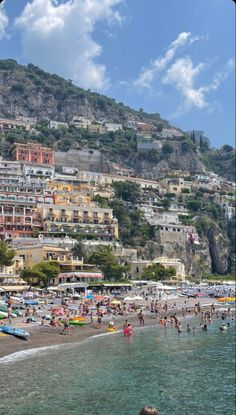 many people are on the beach and in the water near some buildings that have been built into the hillside