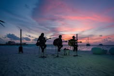 three people playing instruments on the beach at sunset