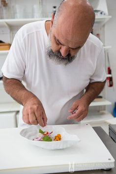 a man in a white shirt preparing food on a cutting board with a knife and fork