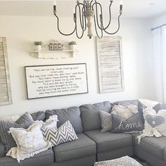 a living room with gray couches and pillows on the floor in front of a chandelier