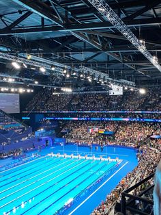 an indoor swimming pool filled with lots of people sitting in the bleachers and watching