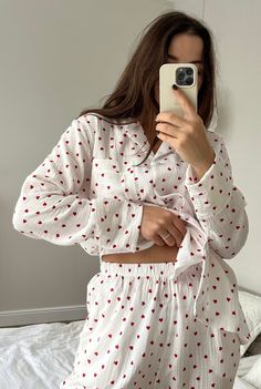 a woman taking a selfie with her cell phone in front of her, wearing a white and red polka dot pajama set