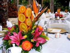 an arrangement of oranges and pink flowers on a table at a wedding or party