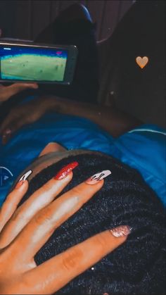 a woman with red and white nails laying on top of a bed next to a cell phone