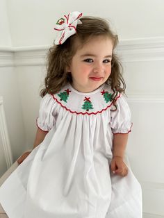 PRE-ORDER - SHIPPING IN NOVEMBER. ESTIMATE DELIVERY DATE PLEASE READ: If you are ordering in stock items along with PRE-ORDER items, they will ship on the PRE-ORDER listing date. If you need the in stock item earlier, please place a separate order.  A sweet winter themed pattern of bows, wreaths, and trees with pink smocking and white satin bows to top off this holiday season's outfit! Clothing Care Instructions: Machine wash gentle. Do not bleach. Tumble dry delicate at low heat. Iron at medium.  Follow us on Instagram @thelillieandlilahshop for shop discounts and updates! White Embroidered Holiday Dress, White Embroidered Dress For Holidays, White Short Sleeve Holiday Dress, White Short Sleeve Dress For Holidays, Short Sleeve Christmas Holiday Dress, Short Sleeve Holiday Dresses For Christmas, Holiday Dresses With Smocked Back, Festive Short Sleeve Holiday Dress For Christmas, Cute White Holiday Dress For Festive Occasions