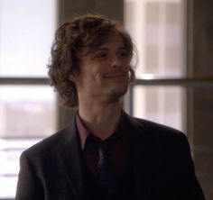 a man with curly hair wearing a suit and tie in an office building looking to his left