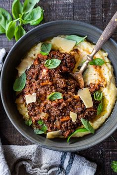 a bowl filled with mashed potatoes topped with meat and cheese, garnished with basil leaves