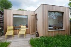 two yellow chairs sitting on top of a wooden deck next to a small building with windows