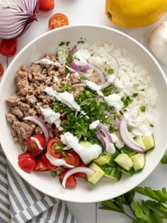 a white bowl filled with rice, meat and veggies on top of a table