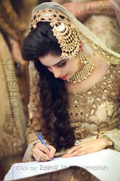 a woman in a bridal gown writing on a piece of paper with a pen