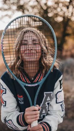 a woman holding a tennis racquet on top of her head in front of trees