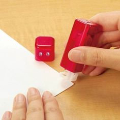 a person is holding a red object in front of a piece of paper and another item on the table