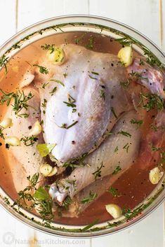 a whole chicken in a pot with herbs and spices on the side, ready to be cooked