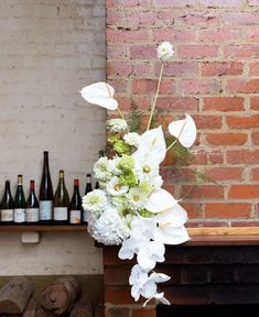 a vase with white flowers and greenery in front of a brick wall filled with wine bottles