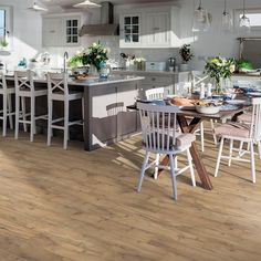 a kitchen filled with lots of white furniture and wooden flooring on top of a hard wood floor