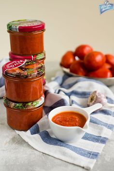 three jars of tomato sauce on a towel next to bowls of tomatoes and other vegetables