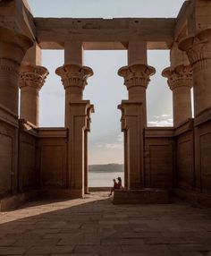 two people are sitting on pillars in the middle of an open area with water behind them