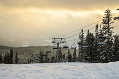 a ski lift with trees and snow on the ground in front of it at sunset