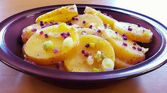 a purple bowl filled with potatoes and garnishes on top of a wooden table