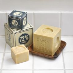 two blocks of soap sitting on top of a wooden tray in front of a white tiled wall