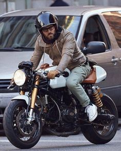 a man riding on the back of a motorcycle down a street next to parked cars