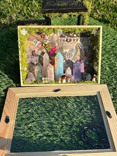 a wooden box sitting on top of a grass covered field next to a mirror with pictures in it