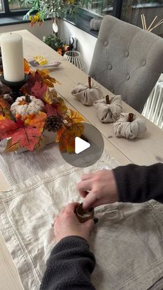 a person sitting at a dining room table with fall leaves on the table and candles