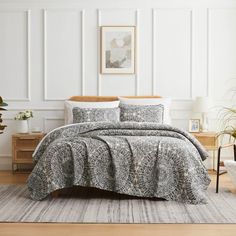 a bedroom with white walls and wooden flooring has a gray comforter on the bed