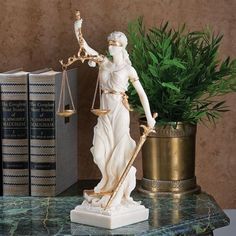 a statue of lady justice on a marble table with books and a potted plant