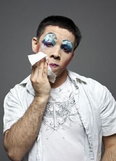 a man with makeup on his face is holding a napkin in front of his face